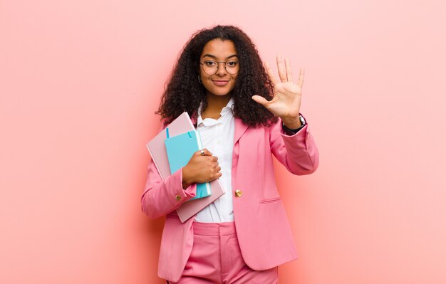 Jeune jolie femme d'affaires avec des livres contre le mur rose