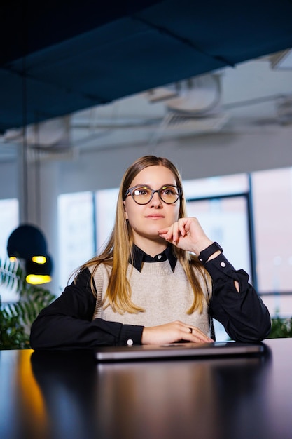 Jeune jolie femme d'affaires à lunettes travaillant au bureau devant un ordinateur portable, travail en ligne