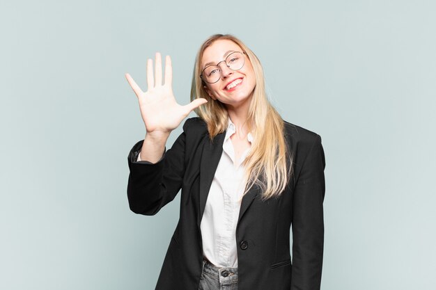 Jeune jolie femme d'affaires souriante et semblant amicale, montrant le numéro cinq ou cinquième avec la main vers l'avant, compte à rebours