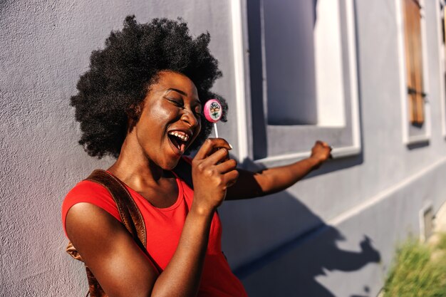 Jeune jolie femme africaine souriante debout à l'extérieur et tenant la sucette.