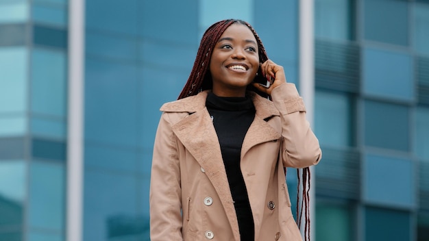 Jeune jolie femme afro-américaine positive debout sur fond d'immeuble de bureaux parlant