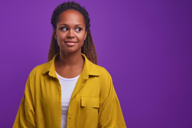 Jeune jolie femme afro-américaine positive regarde ailleurs avec un sourire timide