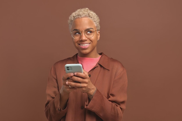 Jeune jolie femme afro-américaine timide avec téléphone dans les mains lève les yeux rêveusement