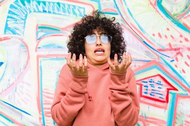 Jeune jolie femme afro désespérée et frustrée, stressée, malheureuse et agacée, criant et hurlant contre le mur de graffitis