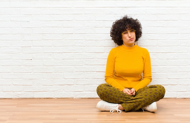 Jeune jolie femme afro à la recherche de plaisir et de convivialité, souriant et un clin d'œil à vous avec une attitude positive assis sur le sol