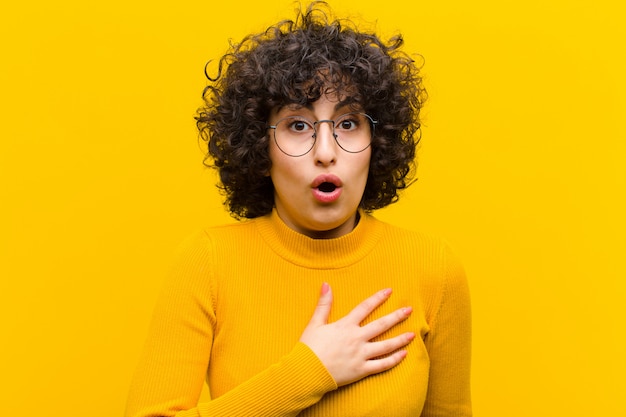 Jeune jolie femme afro se sentant choquée et surprise, souriante, prenant la main à cœur, heureuse d'être la seule ou de montrer sa gratitude