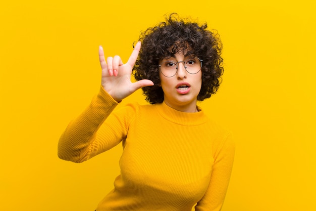 Jeune jolie femme afro se sentant heureuse, amusante, confiante, positive et rebelle, faisant du rock ou du heavy metal signe avec la main