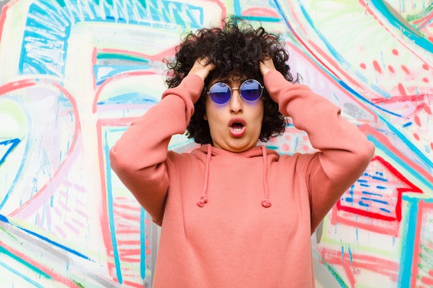 Photo jeune jolie femme afro se sentant horrifiée et choquée, levant les mains pour se diriger et paniquant devant une erreur sur un mur de graffitis