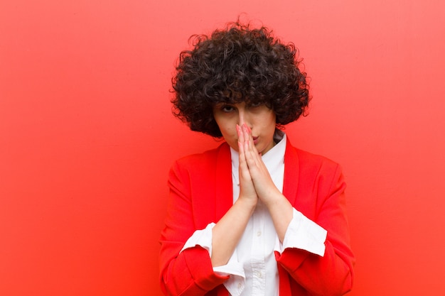 Photo jeune jolie femme afro se sentant inquiète, pleine d'espoir et religieuse, priant fidèlement avec ses paumes pressées, demandant pardon