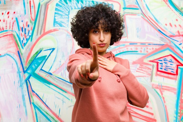 Jeune jolie femme afro souriante fière et confiante de prendre la première pose triomphale, se sentir comme un leader contre un mur de graffitis