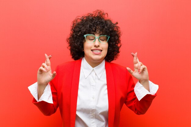 Jeune jolie femme afro souriante et qui croise anxieusement les deux doigts, inquiète et souhaite ou espère avoir de la chance