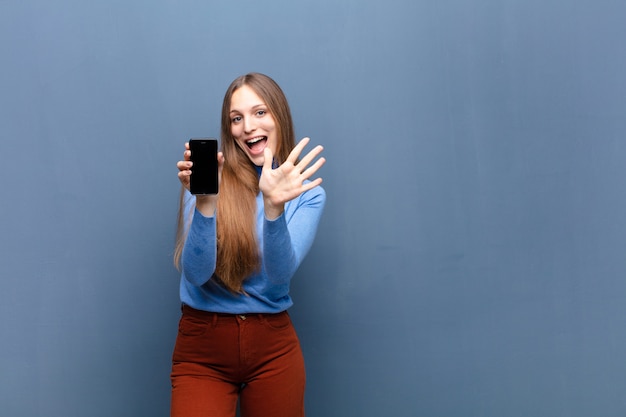 Photo jeune jolie femme à l'aide d'un mur bleu de téléphone intelligent avec une surface