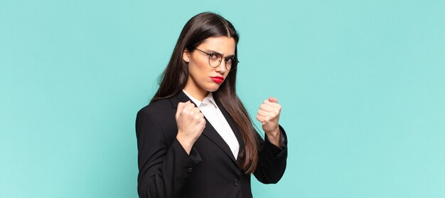 Jeune jolie femme à l'air confiante, en colère, forte et agressive, avec les poings prêts à se battre en position de boxe. concept d'entreprise