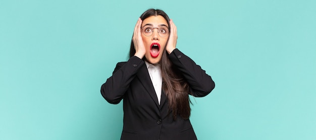 jeune jolie femme à l'air désagréablement choquée, effrayée ou inquiète, la bouche grande ouverte et couvrant les deux oreilles avec les mains. concept d'entreprise