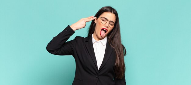 Jeune jolie femme à l'air malheureuse et stressée, geste de suicide faisant un signe d'arme à feu avec la main, pointant vers la tête. concept d'entreprise