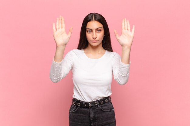 Jeune jolie femme à l'air sérieuse, malheureuse, en colère et mécontente interdisant l'entrée ou disant stop avec les deux paumes ouvertes