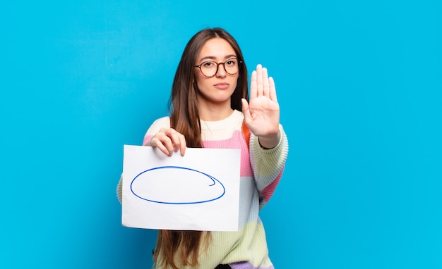 Jeune jolie femme à l'air sérieuse, sévère, mécontente et en colère montrant la paume ouverte faisant un geste d'arrêt