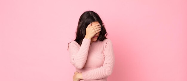 Jeune jolie femme à l'air stressée, honteuse ou contrariée, avec un mal de tête, couvrant le visage avec la main