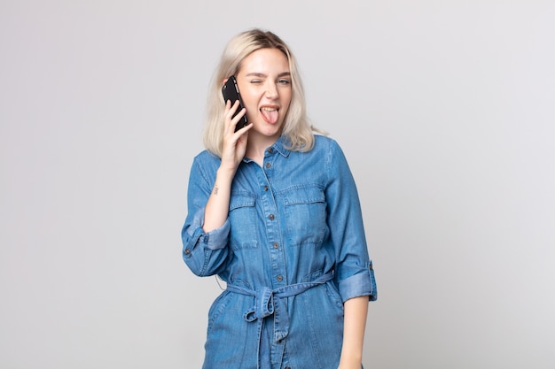 Jeune jolie femme albinos avec une attitude joyeuse et rebelle, plaisantant et tirant la langue et parlant avec un smartphone