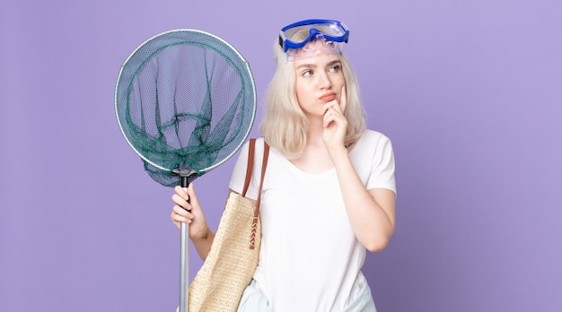 Jeune jolie femme albinos pensant, se sentant dubitative et confuse avec des lunettes et un filet de pêche