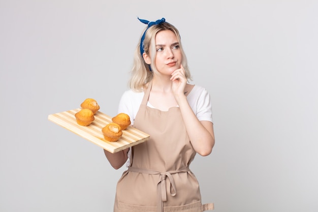 Jeune jolie femme albinos pensant, se sentant dubitative et confuse avec un plateau à muffins