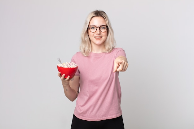 Jeune jolie femme albinos pointant sur la caméra vous choisissant avec un bol de petit-déjeuner