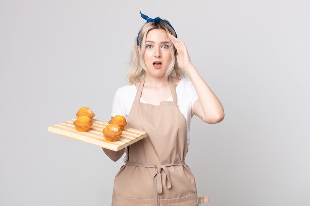Jeune jolie femme albinos à la recherche d'heureux, étonné et surpris avec un plateau de muffins