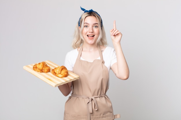 Jeune jolie femme albinos se sentant comme un génie heureux et excité après avoir réalisé une idée avec un plateau de croissants