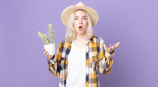 Jeune jolie femme albinos se sentant extrêmement choquée et surprise et tenant un cactus de plante d'intérieur