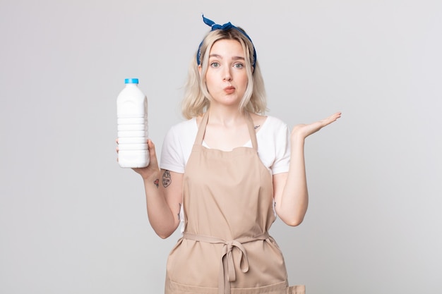 Jeune jolie femme albinos se sentant perplexe et confuse et doutant avec une bouteille de lait