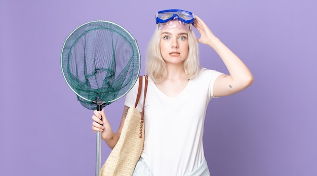 Jeune jolie femme albinos se sentant stressée, anxieuse ou effrayée, les mains sur la tête avec des lunettes et un filet de pêche