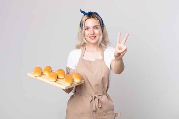 Jeune jolie femme albinos souriante et semblant heureuse, gesticulant la victoire ou la paix avec un plateau de petits pains