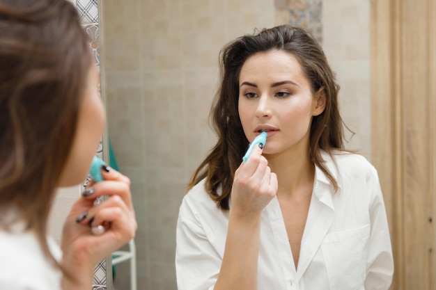 Photo une jeune jolie femme applique du rouge à lèvres devant un miroir beauté propreté santé et soins