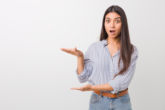 Jeune jolie femme arabe choquée et émerveillée tenant un espace copie entre les mains.