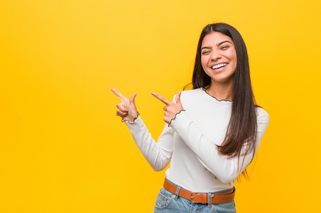 Jeune jolie femme arabe sur un fond jaune pointant avec les index sur un espace de copie, exprimant l&#39;enthousiasme et le désir.