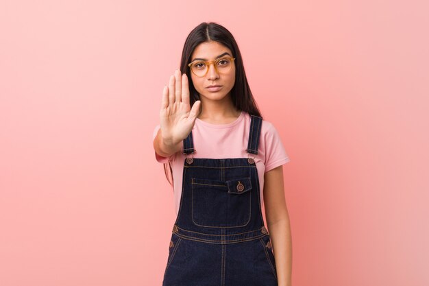 Jeune jolie femme arabe portant une salopette jeans debout avec la main tendue montrant le panneau d'arrêt, vous empêchant.