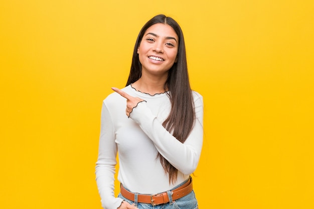 Jeune jolie femme arabe souriante et pointant de côté, montrant quelque chose dans un espace vide.