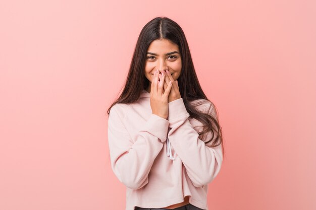 Jeune jolie femme arabe vêtue d&#39;un look sport décontracté qui rit, qui se couvre la bouche avec les mains.