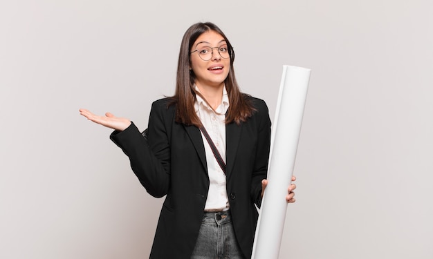 Jeune jolie femme architecte se sentant heureuse, surprise et joyeuse, souriante avec une attitude positive, réalisant une solution ou une idée