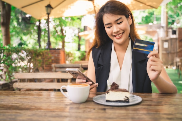 Jeune jolie femme asiatique heureuse utilise une tablette ou un smartphone pour faire des achats et payer en ligne par carte de débit ou de crédit