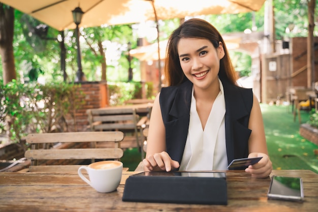 Jeune jolie femme asiatique heureuse utilise une tablette ou un smartphone pour faire des achats et payer en ligne par carte de débit ou de crédit