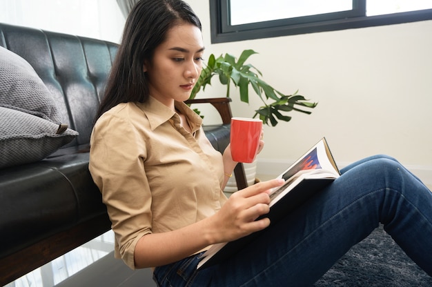 Jeune jolie femme asiatique peau blanche assise boire du café et lire un livre bénéficie de repos