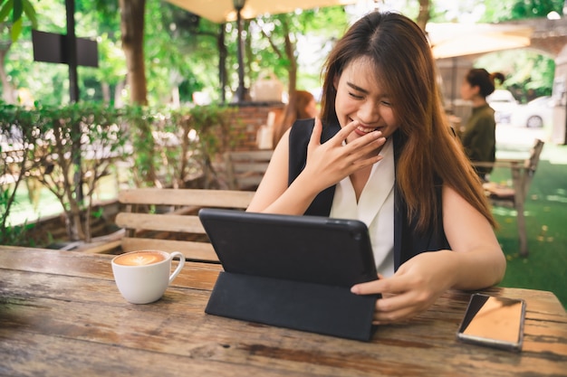 Jeune jolie femme asiatique à se sentir heureux utilise une tablette dans le magasin de café
