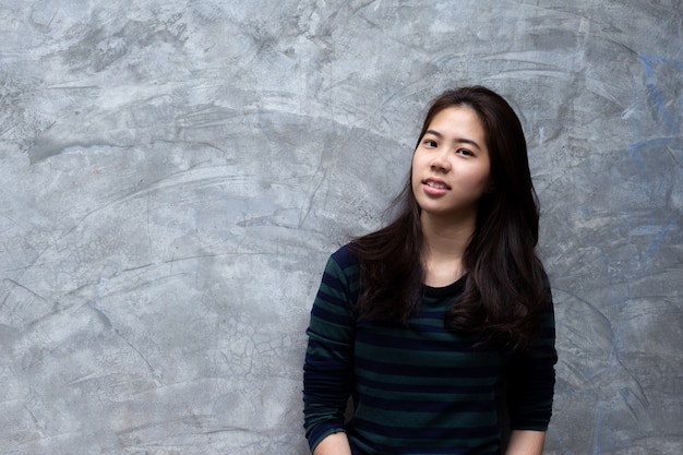 Jeune jolie femme asiatique souriante sur fond de mur en béton gris.