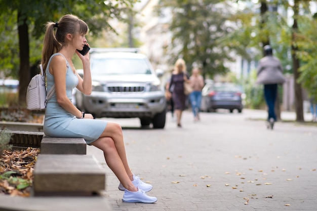 Jeune jolie femme assise sur un banc parlant sur son téléphone portable à l'extérieur dans la rue de la ville