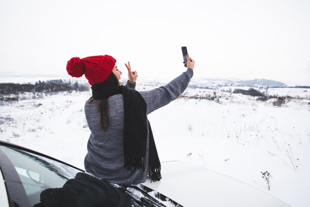 Jeune jolie femme assise sur le capot de la voiture et prenant selfie. voyage en voiture hors route. mode de vie