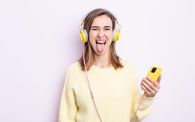 Jeune jolie femme à l'attitude joyeuse et rebelle, plaisantant et tirant la langue. casque et concept de téléphone