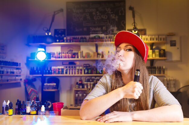 Jeune jolie femme au bonnet rouge fume une cigarette électronique chez vape shop