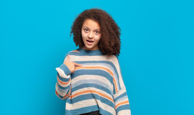 Jeune jolie femme aux cheveux afro et pull rayé posant sur le mur bleu