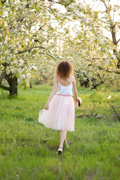 Jeune jolie femme aux cheveux bouclés marchant dans un jardin fleuri vert. Humeur romantique de printemps